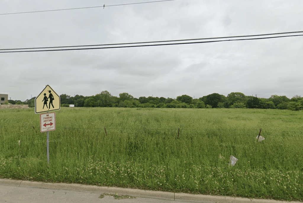 A grassy field with a 'School Crossing' sign and a 'No Parking Anytime' sign, set against a cloudy sky.