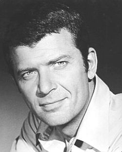 Black and white portrait of a man with short hair, wearing a light-colored shirt, looking directly at the camera with a slight smile.
