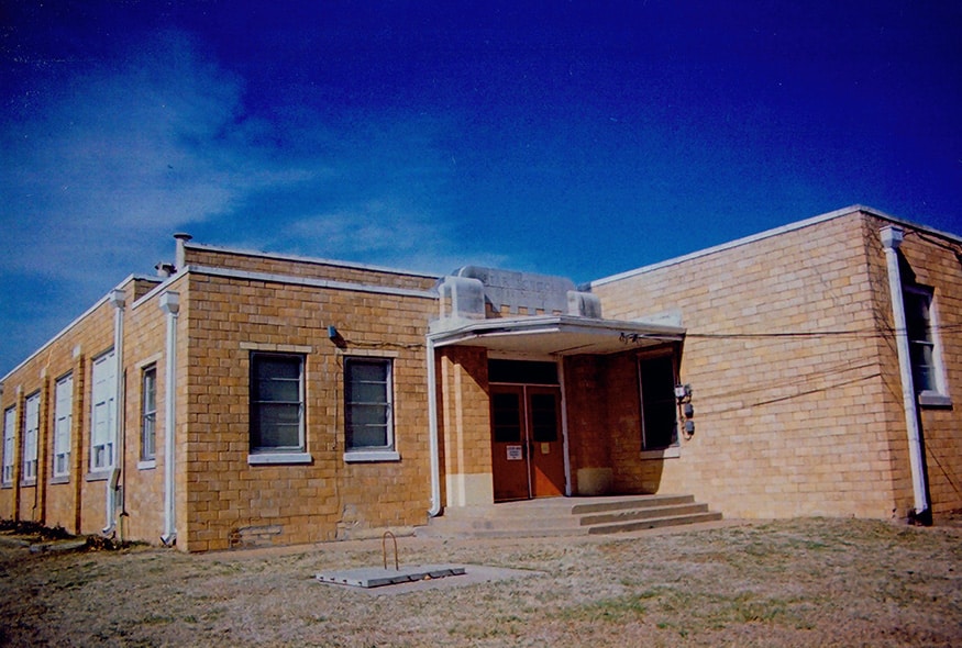 Exterior view of a historic building made of stone, featuring a front entrance with steps and windows, against a clear blue sky.