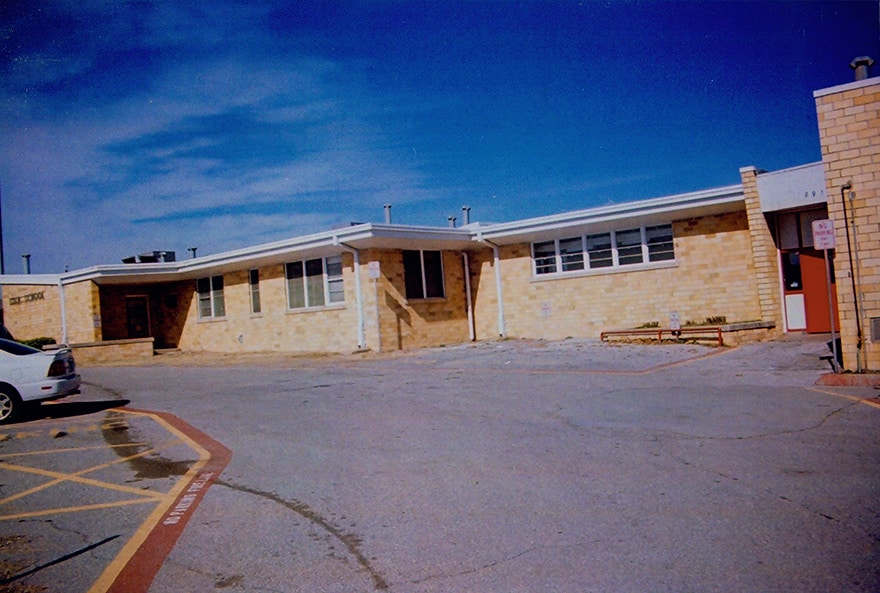 Exterior view of a single-story brick building with multiple windows, a parking lot, and a clear blue sky.