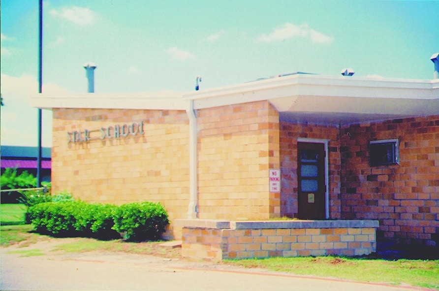 Exterior view of the STAR School building, featuring a brick facade, a flat roof, and a 'No Parking' sign. Lush greenery is visible in front of the building under a clear blue sky.