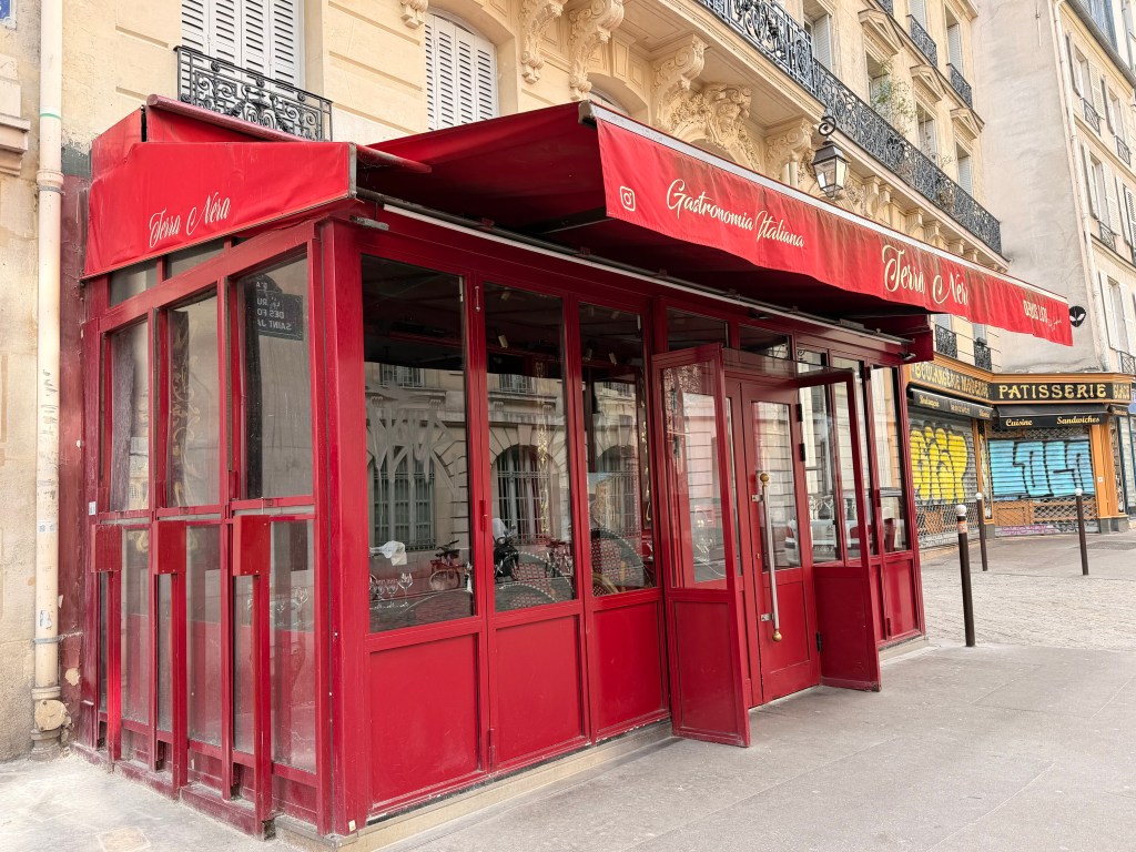 Exterior view of a red Italian restaurant with large glass windows and awnings, located on a street corner.