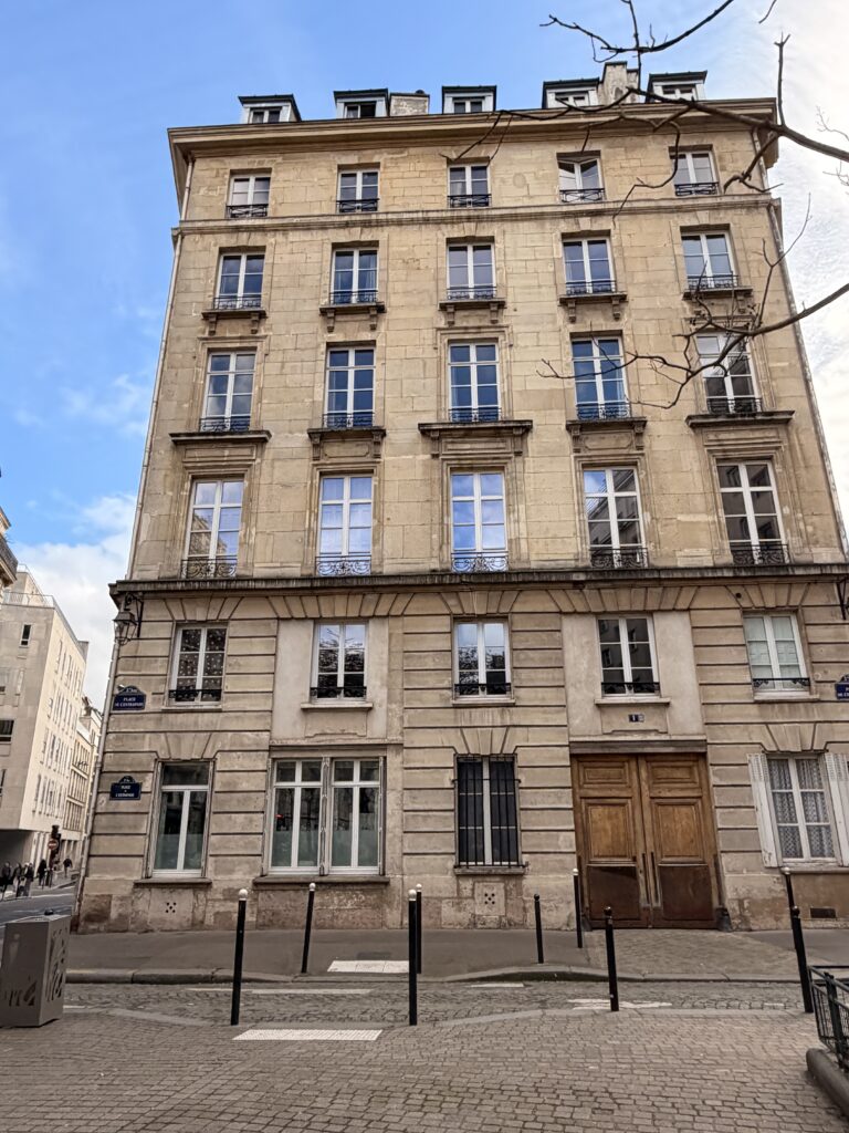 A classic Parisian building with multiple windows and traditional architectural details, set against a blue sky.